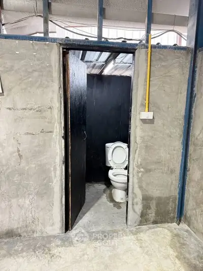Industrial-style bathroom with concrete walls and exposed piping, featuring a basic toilet setup.