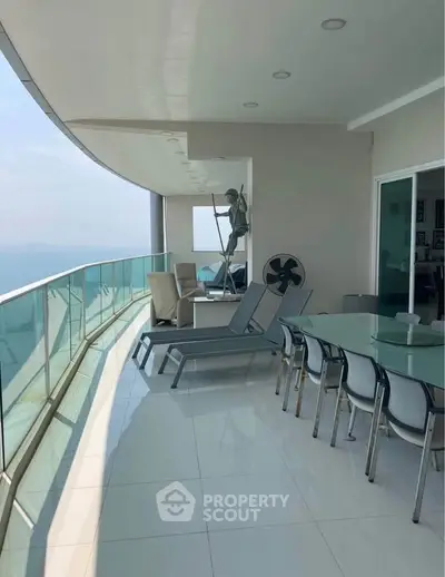 Luxurious balcony with stunning ocean view, modern furniture, and sleek glass railing in high-rise apartment.