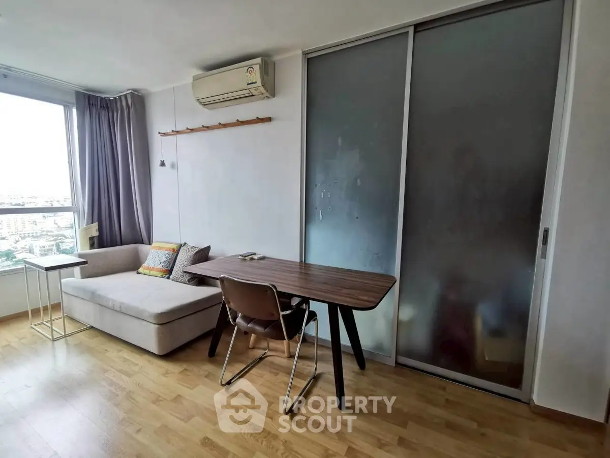 Modern living room with sleek furniture and large window offering city view.