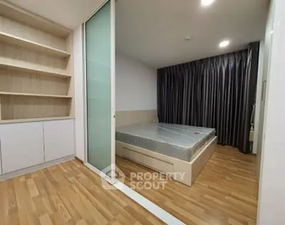 Modern bedroom with wooden flooring and built-in shelves, featuring a sliding glass door.