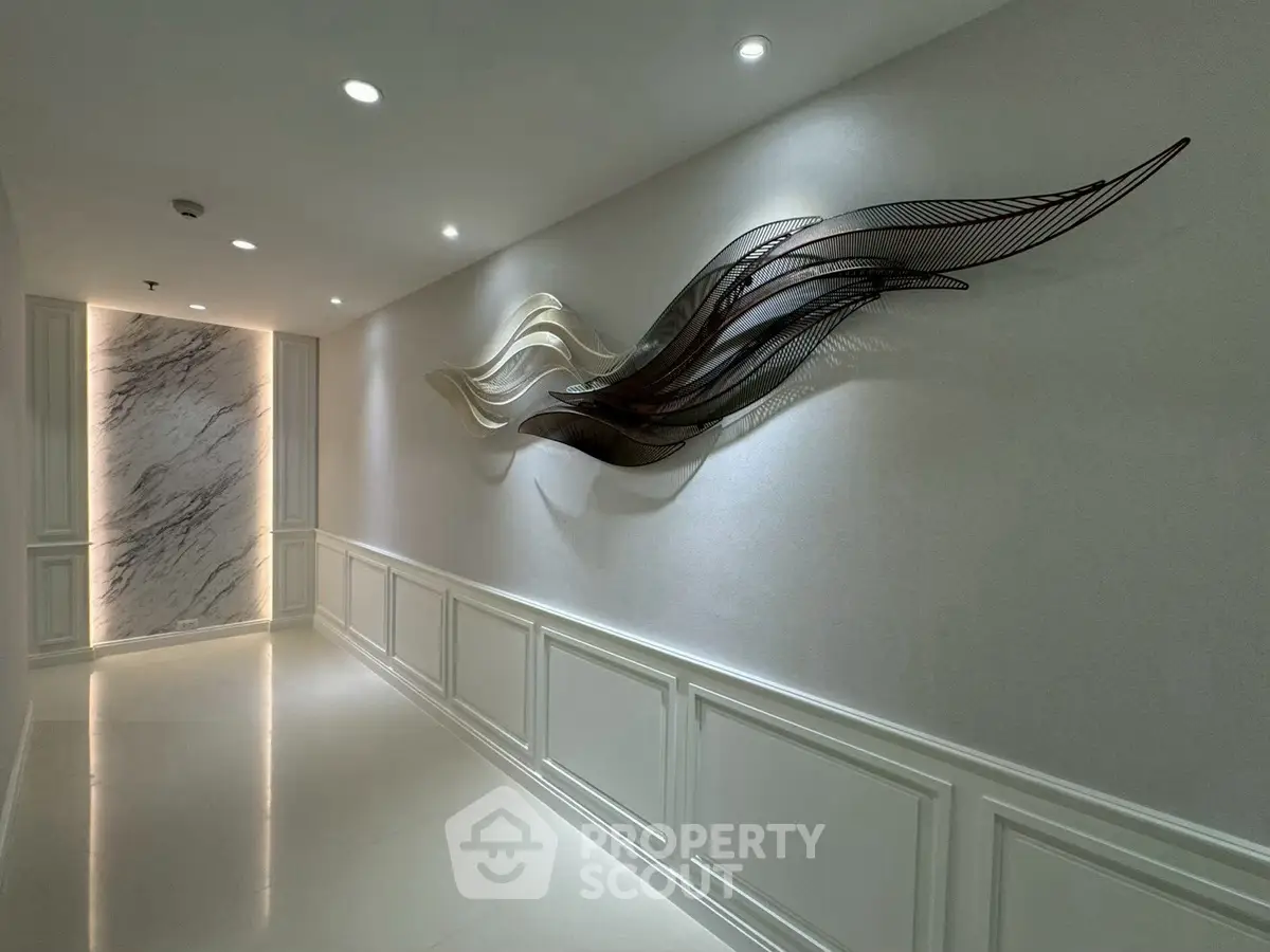 Elegant hallway with modern art and marble accent wall in luxury building.