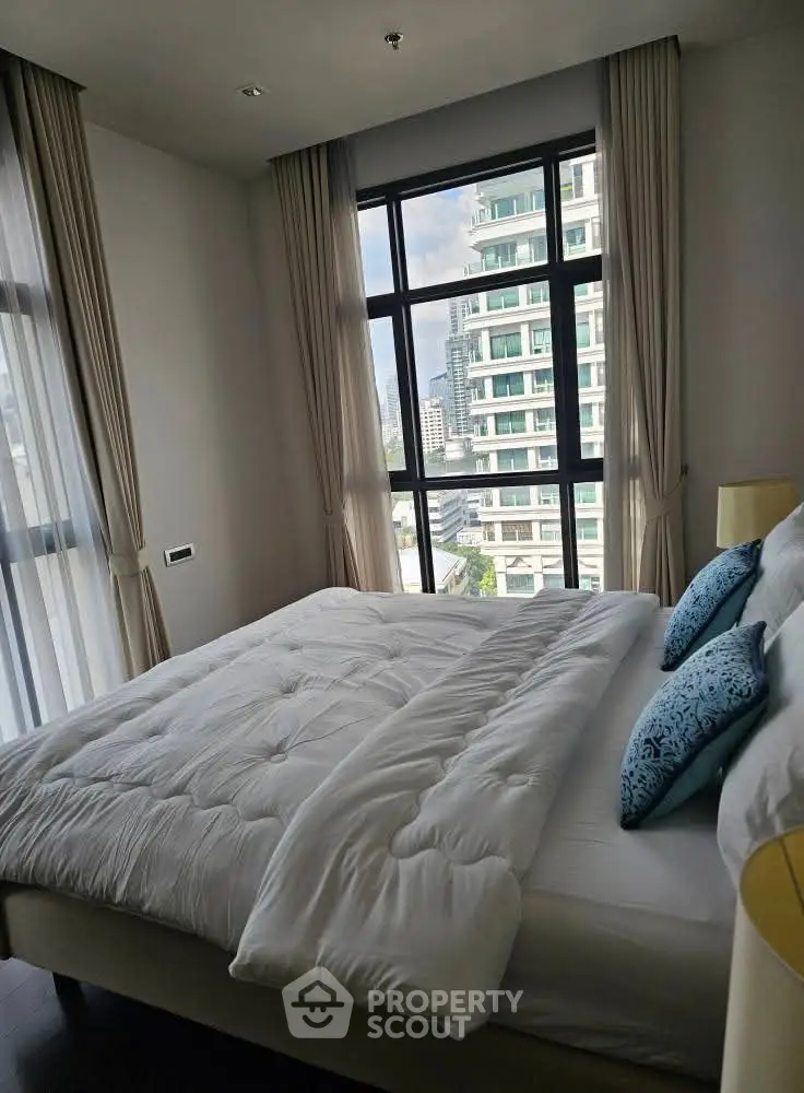 Modern bedroom with large windows offering a stunning city view, featuring elegant curtains and plush bedding.