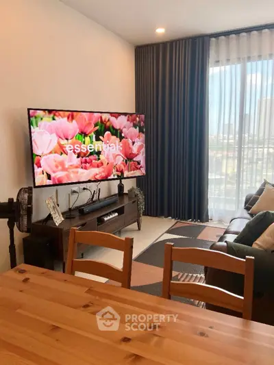 Modern living room with large TV and stylish decor, featuring a cozy seating area and natural light.