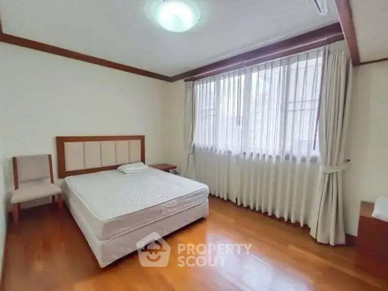 Spacious bedroom with wooden flooring and large window for natural light.