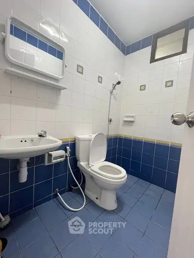 Compact bathroom with blue and white tiles, featuring a toilet, sink, and shower.