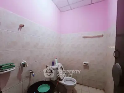 Cozy bathroom with pink walls and tiled design, featuring essential fixtures and a modern toilet.