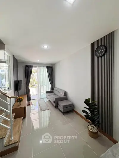 Modern living room with sleek design, featuring a gray sofa, wall clock, and large windows for natural light.