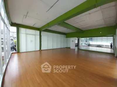 Spacious open room with wooden flooring and large windows, ideal for versatile use.