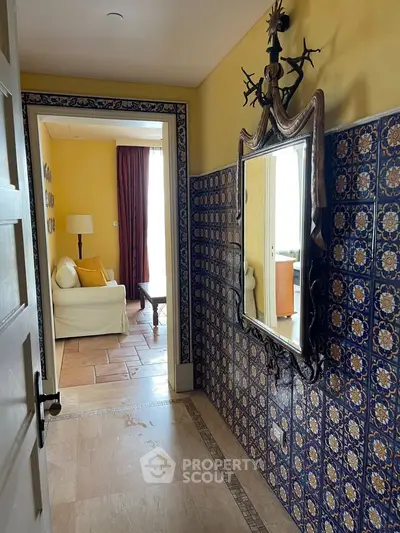 Charming hallway with ornate mirror and tiled walls leading to cozy living room with natural light.