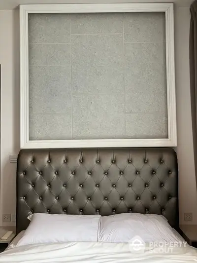 Elegant bedroom featuring a luxurious tufted headboard and crisp white bedding, complemented by a large window with stylish gray tiling.