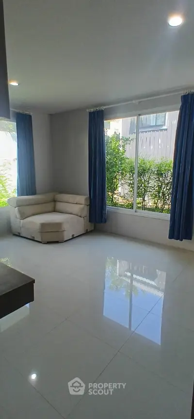 Bright living room with large window and modern white sofa, offering a serene garden view.