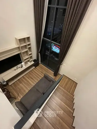 Modern loft-style living room with high ceilings and large windows offering city views.