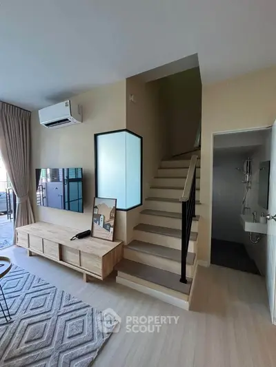 Modern living room with staircase and stylish decor, featuring natural light and contemporary design.