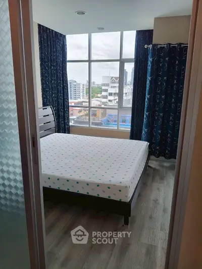 Bright bedroom with large window offering city view, featuring a comfortable bed and stylish curtains.
