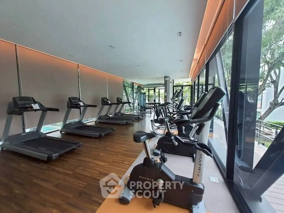 Modern gym with state-of-the-art equipment and floor-to-ceiling windows offering lush garden views.