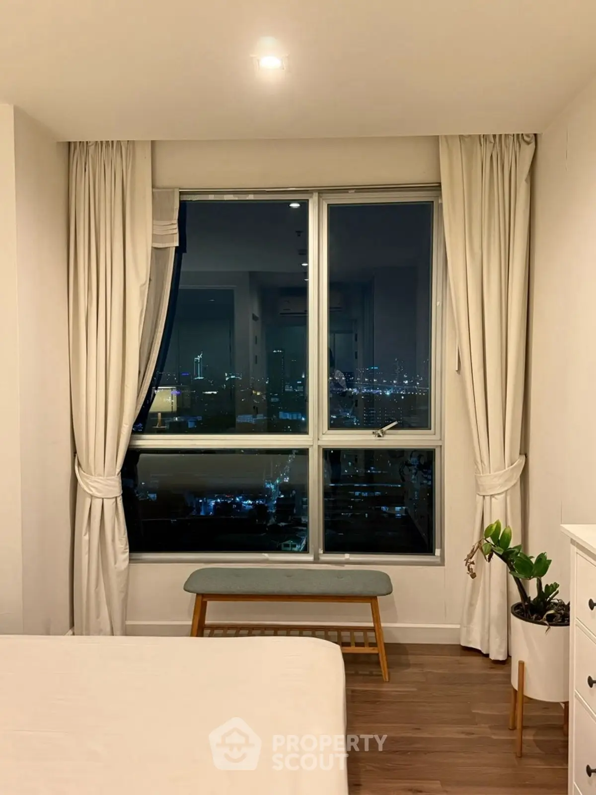 Cozy bedroom with large window offering stunning night city view, elegant curtains, and stylish decor.