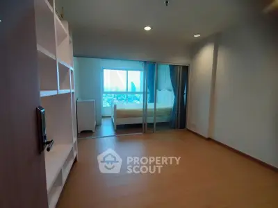 Spacious bedroom with wooden flooring and city view, featuring a sliding glass door and built-in shelves.