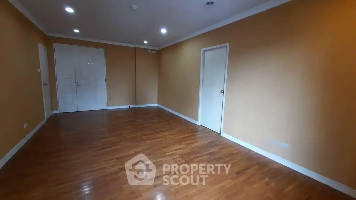 Spacious empty room with wooden flooring and beige walls, ideal for customization.