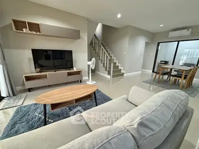 Modern living room with stylish furniture and open dining area, featuring sleek staircase and neutral tones.