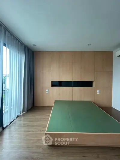 Spacious modern bedroom with wooden flooring and large windows for natural light.