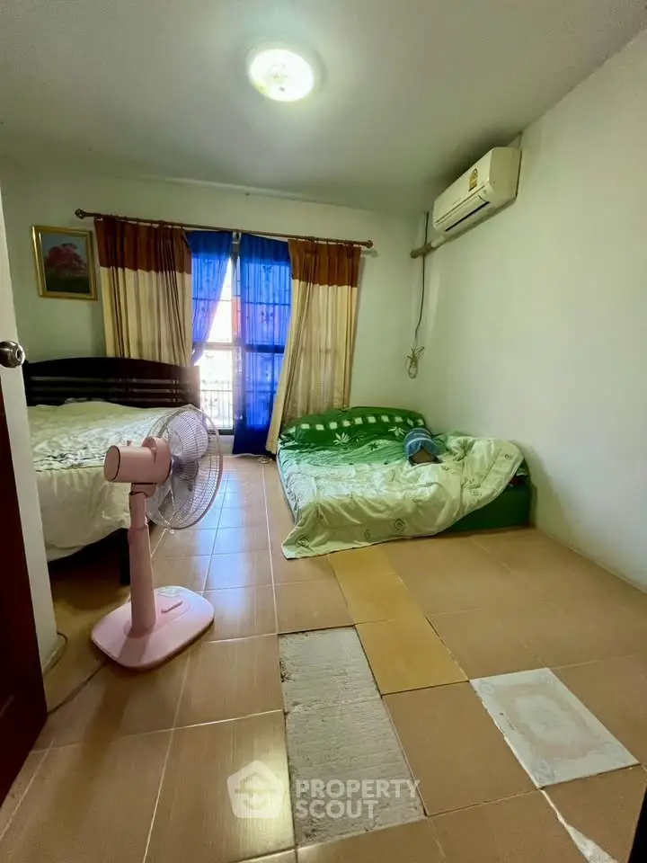 Cozy bedroom with two beds, air conditioning, and natural light from a window with colorful curtains.