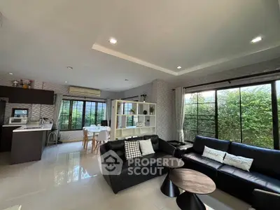 Spacious modern living room with open kitchen and large windows overlooking greenery.