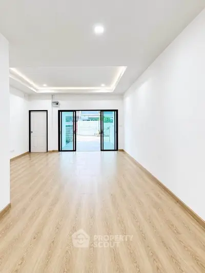 Spacious modern living room with wooden flooring and large glass doors leading to a balcony.