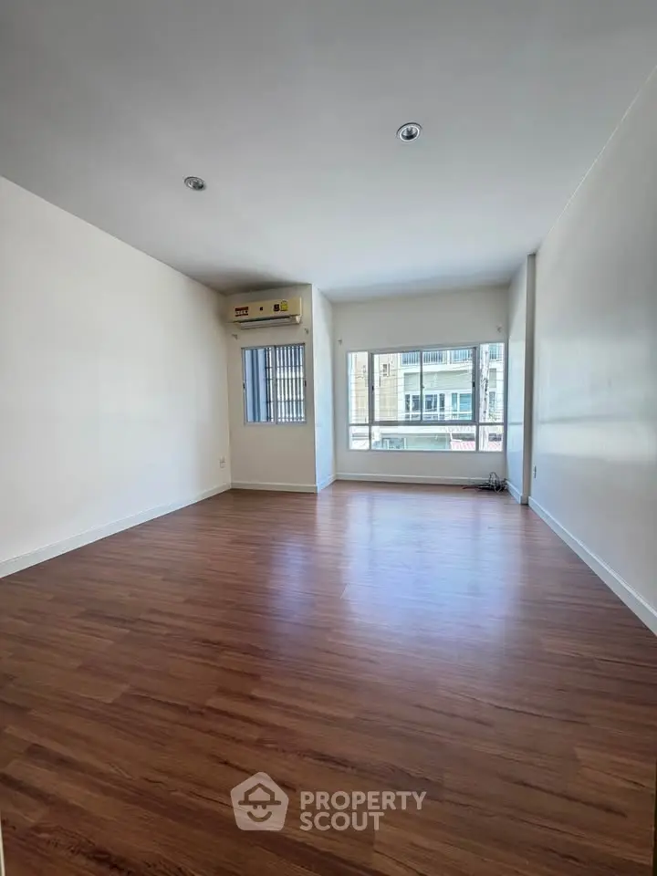 Spacious empty living room with wooden flooring and large window offering natural light.