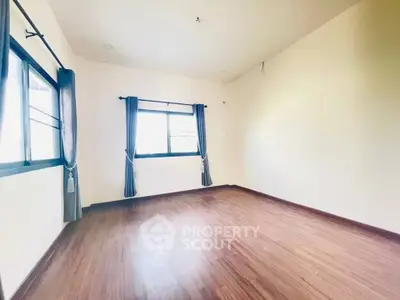 Spacious empty room with wooden flooring and large windows for natural light.