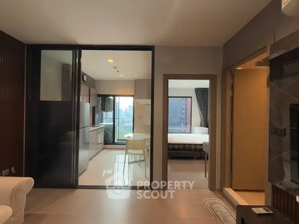 Modern open-plan living space with kitchen and bedroom view, featuring sleek design and natural light.