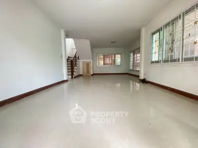 Spacious empty living room with large windows and staircase, perfect for customization.