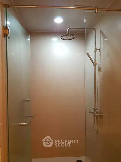 Modern shower area with glass door and overhead rain shower in sleek bathroom.