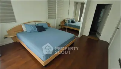 Spacious bedroom with wooden flooring and large mirror closet in modern apartment.