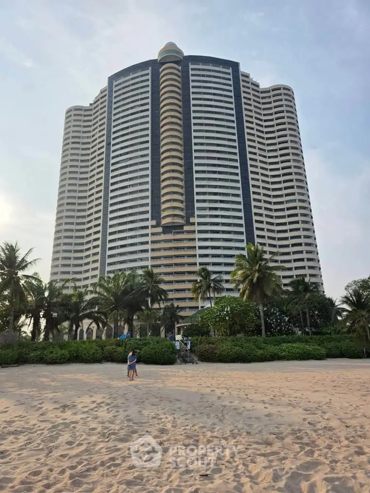 Stunning beachfront high-rise building with lush palm trees and sandy beach, perfect for luxury living.