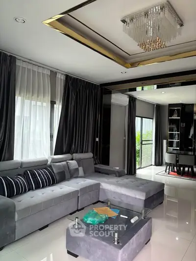 Luxurious modern living room with elegant chandelier and plush gray sectional sofa.