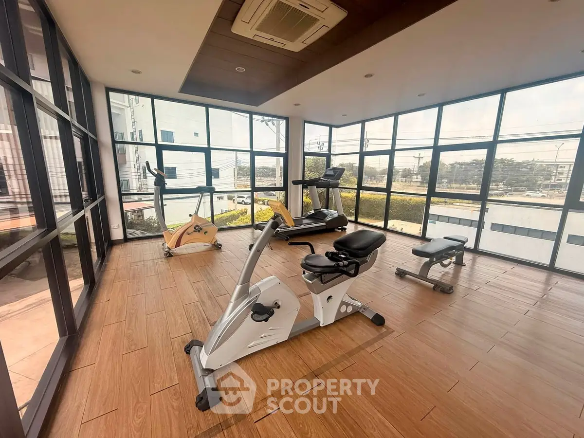 Modern gym with large windows and exercise equipment in a bright, spacious room.