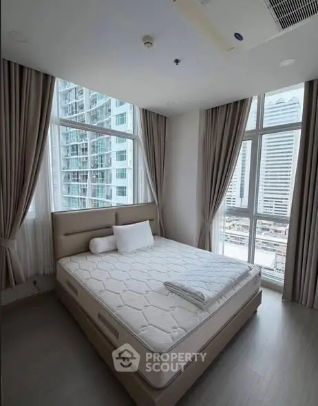 Modern bedroom with large windows and city view in a high-rise apartment.