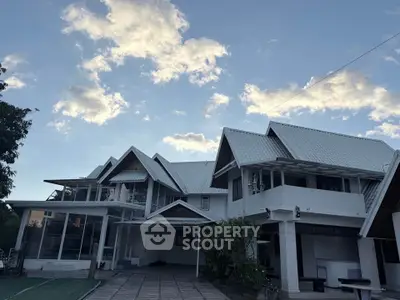 Stunning multi-gabled white house with expansive driveway and lush greenery under a picturesque sky.