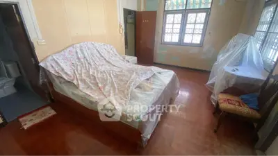 Cozy bedroom with wooden flooring and natural light, featuring a covered bed and vintage decor.