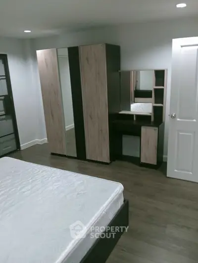 Modern bedroom with sleek wardrobe and vanity set, featuring wooden flooring and minimalist design.