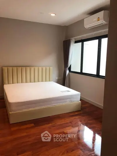 Spacious bedroom with elegant wooden flooring and large window for natural light.