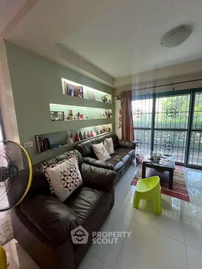Cozy living room with leather sofa and decorative shelves, bright natural light from large window.