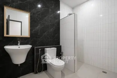 Modern bathroom with sleek black and white tiles, featuring a wall-mounted sink and toilet.