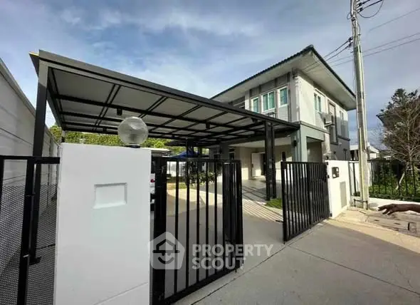 Modern two-story house with gated entrance and carport in a suburban setting.