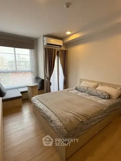 Cozy bedroom with modern furnishings and large window offering city views.