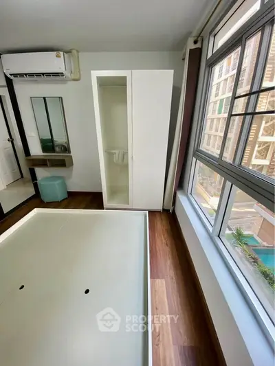 Modern bedroom with large windows and wooden flooring, featuring a sleek wardrobe and air conditioning unit.
