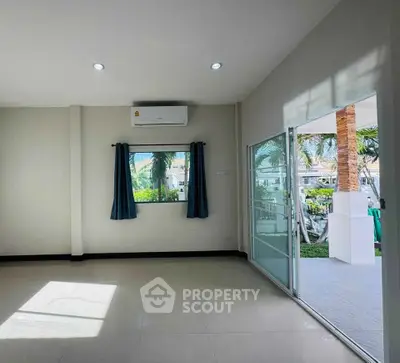 Bright living room with sliding glass doors opening to a garden view, featuring modern air conditioning.