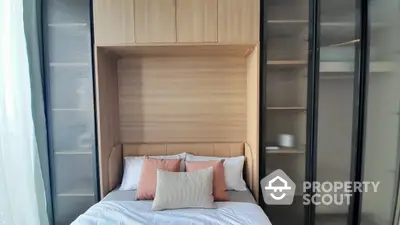 Cozy modern bedroom with built-in wooden headboard and wardrobe, accented with stylish peach pillows, offering a serene and organized living space.