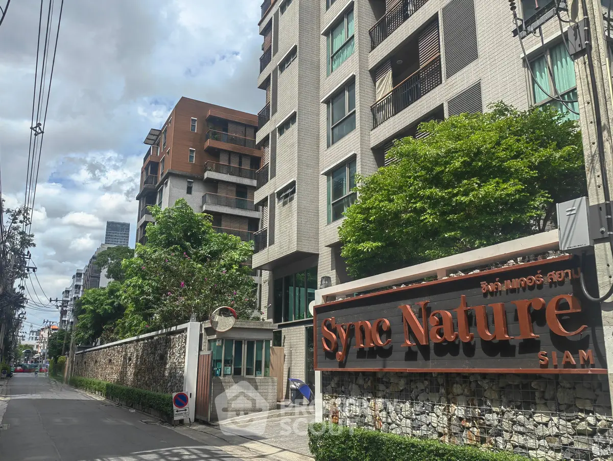 Modern residential building exterior with lush greenery and street view in urban setting.