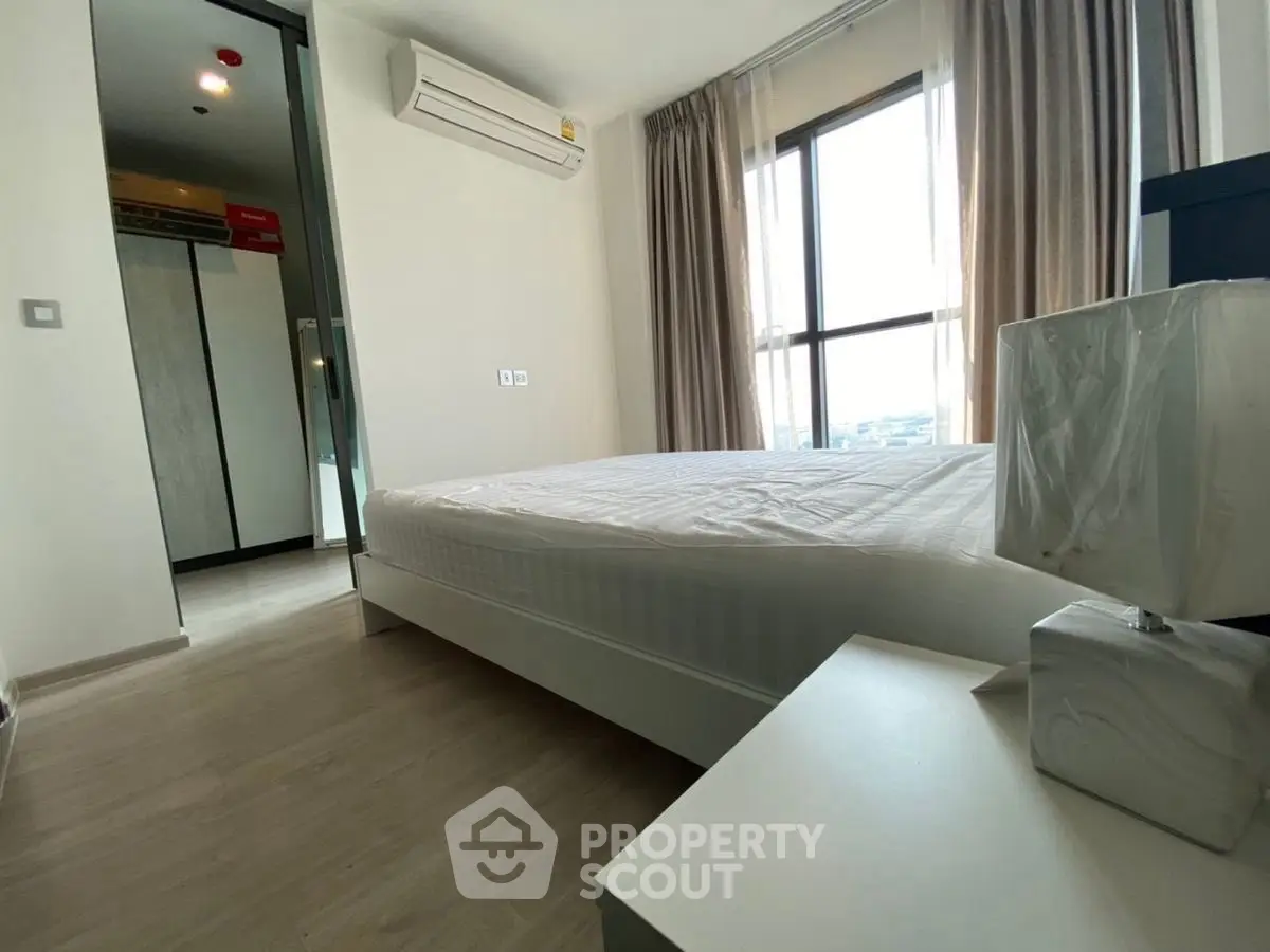 Modern bedroom with large window and minimalist decor in a high-rise apartment.
